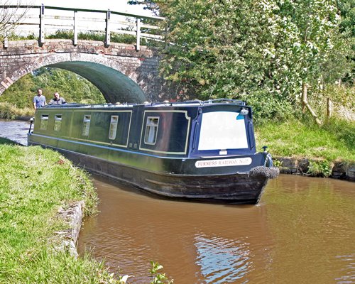 People on a canal boat at the waterfront with a bridge.