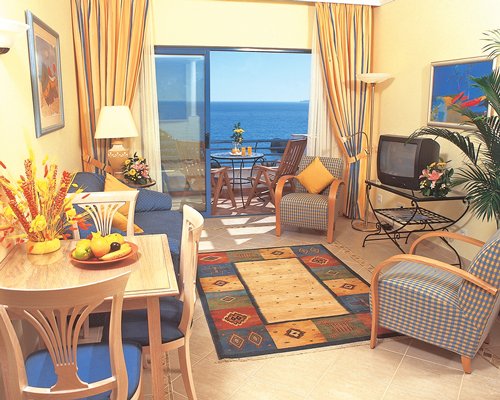 An open plan living room and dining room with a television and a balcony with beach view.