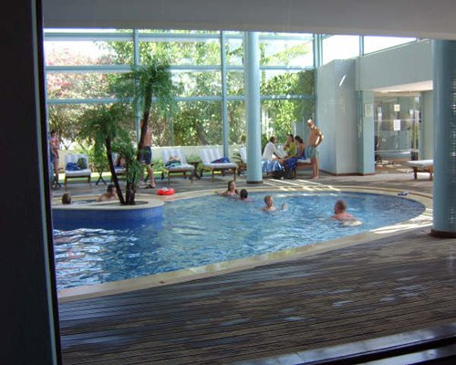 An indoor swimming pool with chaise lounge chairs and an outside view.