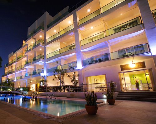 An outdoor swimming pool alongside multi story resort units at night.