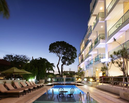 An outdoor swimming pool with chaise lounge chairs at night.