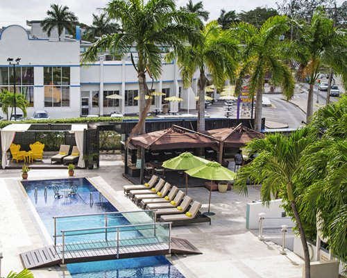 A bridge over an outdoor swimming pool with chaise lounge chairs and sunshades.