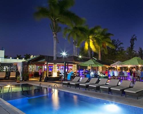 Night view of an outdoor swimming pool with chaise lounge chairs and poolside bars.