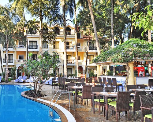 An outdoor swimming pool with chaise lounge chairs alongside fine dining restaurant surrounded by trees.