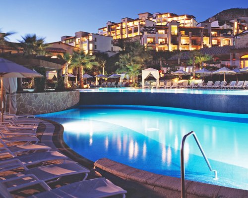 An outdoor swimming pool with chaise lounge chairs alongside the resort at dusk.