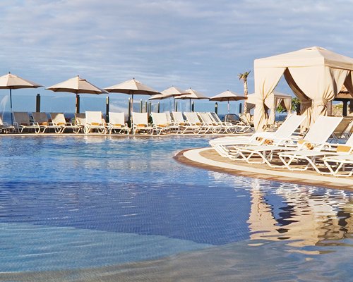 A large outdoor swimming pool with chaise lounge chairs and sunshades.
