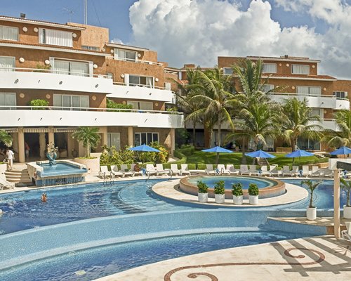 An outdoor swimming pool with chaise lounge chairs and sunshades alongside the multi story resort unit.