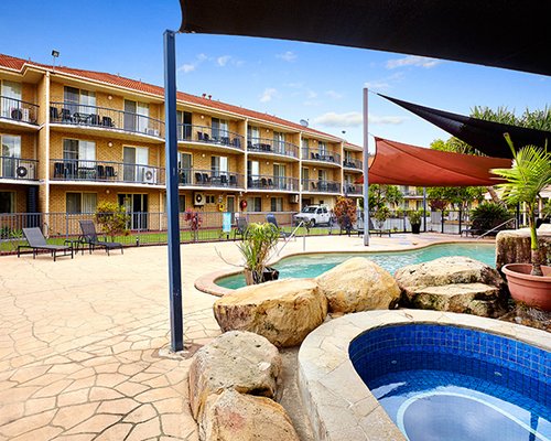 An outdoor swimming pool with hot tub and chaise lounge chairs alongside the multi story unit.