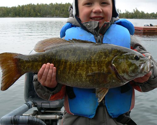 A child holding a fish on a boat at the lake.