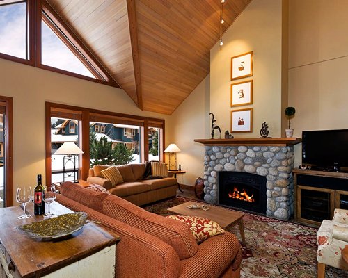 A well furnished living room with a television fire in the stone fireplace and outside view.