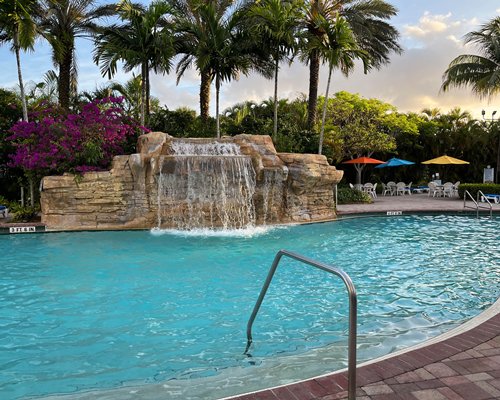 An outdoor swimming pool with waterfall and chaise lounge chairs sunshades.