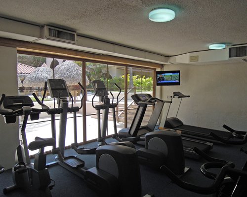 A well equipped indoor fitness center with a television and an outside view.