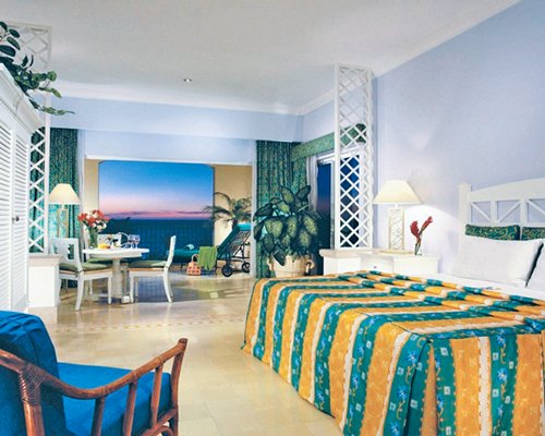 A well furnished bedroom with dining area chaise lounge chairs balcony and ocean view.