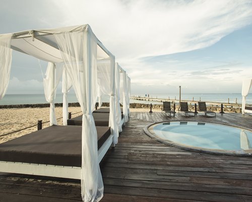 Outdoor hot tub with beach beds and chaise lounge chairs alongside the ocean.