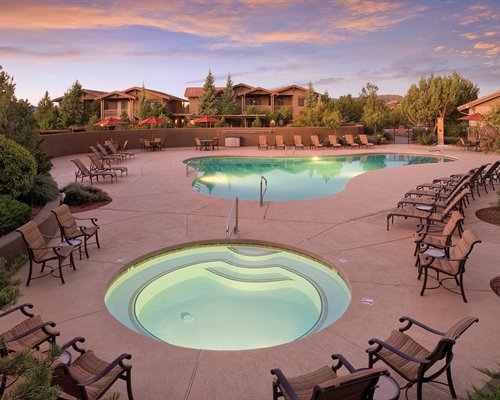 An outdoor swimming pool with hot tub and patio furniture at dusk.