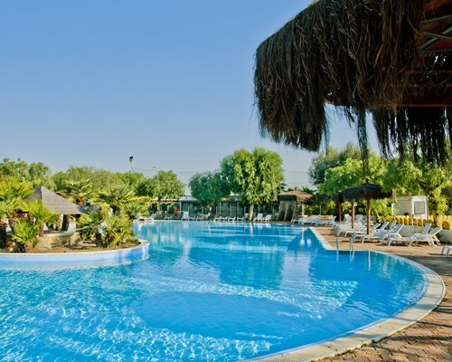 A large outdoor swimming pool with chaise lounge chairs and thatched sunshades.