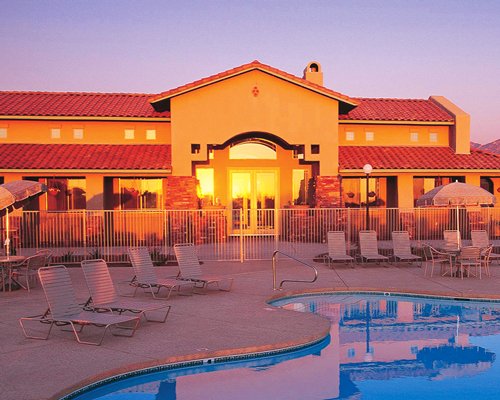 An outdoor swimming pool with chaise lounge chairs and patio furniture alongside the resort at dusk.