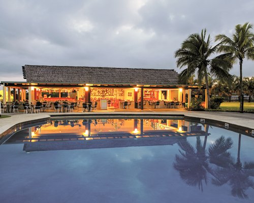 An outdoor swimming pool with a restaurant at dusk.