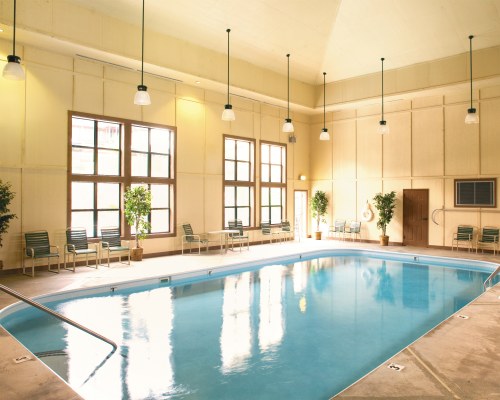 AN INDOOR SWIMMING POOL WITH PATIO FURNITURE AND AN OUTSIDE VIEW.
