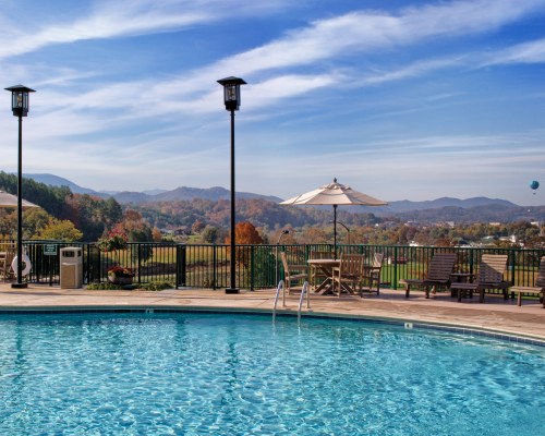 LARGE OUTDOOR SWIMMING POOL WITH PATIO FURNITURE SUNSHADE AND CHAISE LOUNGE CHAIRS.