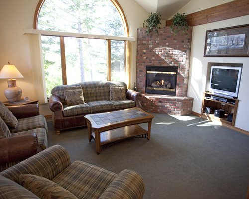 A well furnished living room with a television fire in the fireplace and outside view.