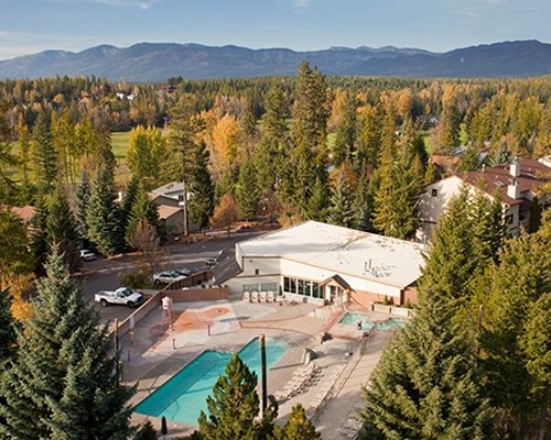 An aerial view of an outdoor swimming pool with chaise lounge chairs surrounded by wooded area.