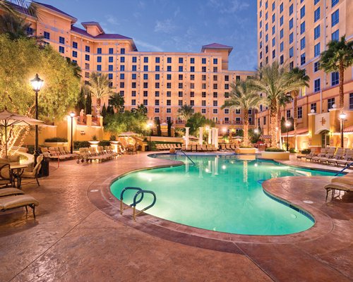 Exterior view of Wyndham Grand Desert with outdoor swimming pool chaise lounge chairs and palm trees.