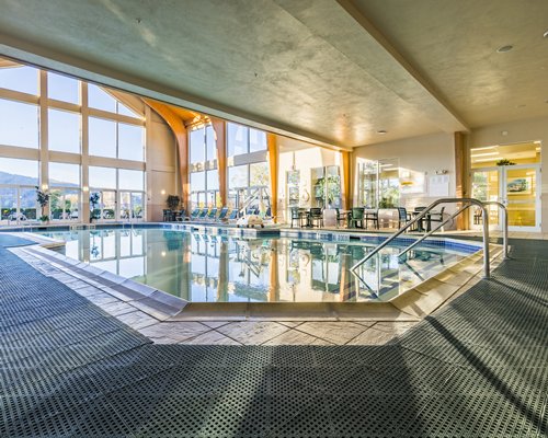 An indoor swimming pool with chaise lounge chairs and an outside view.