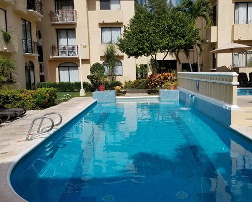 An outdoor swimming pool with lounge chairs and sunshades alongside resort units and the beach.