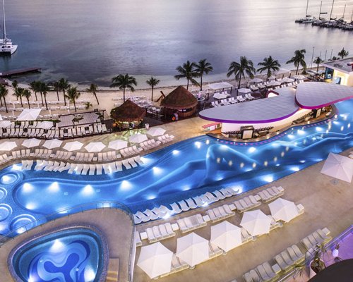 An outdoor swimming pool with hot tub chaise lounge chairs and sunshades alongside the beach.