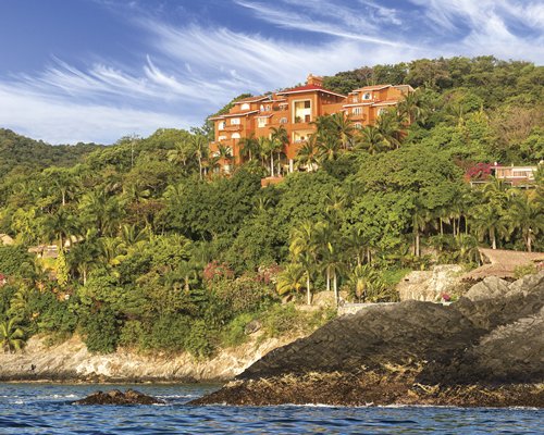 An exterior view of WorldMark Zihuatenejo resort from the beach surrounded by woods.