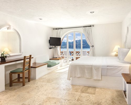 A well furnished bedroom with king bed television balcony patio chairs and ocean view.