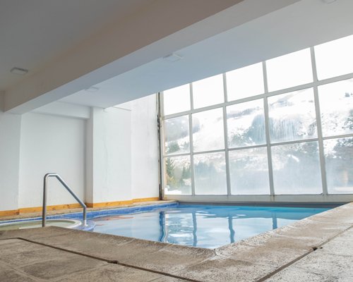 An indoor hot tub with chaise lounge chairs and an outside view.