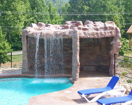 An outdoor pool with water fountain alongside chaise lounge chairs.