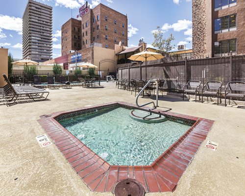 An outdoor hot tub with chaise lounge chairs and sunshades alongside multi story condos.