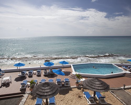 An aerial view of an outdoor swimming pool with chaise lounge chairs alongside the beach.