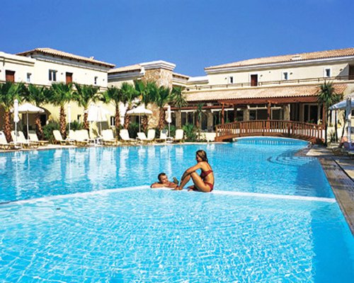 A couple talking in an outdoor swimming pool with chaise lounge chairs alongside resort condos.