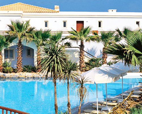 An outdoor swimming pool with chaise lounge chairs umbrellas alongside the resort.
