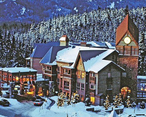 Dusk view of Club Intrawest Whistler resort alongside pine trees covered in snow.