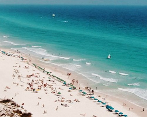An aerial view of gulf waters and the beach with chaise lounge chairs.