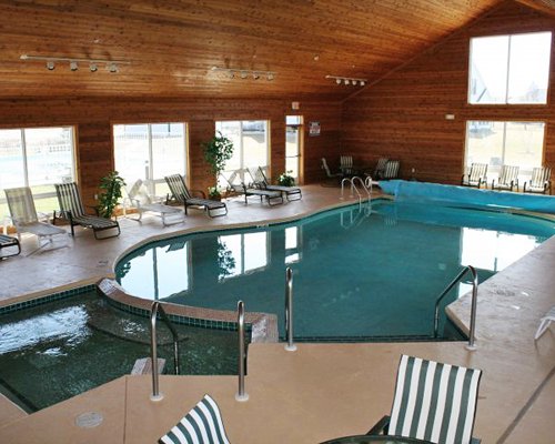 An indoor swimming pool with a hot tub and chaise lounge chairs.
