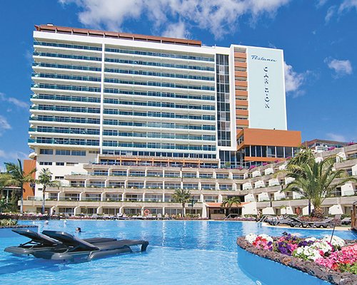 Scenic exterior view of Pestana Carlton Tower Suites with outdoor swimming pool and chaise lounge chairs.