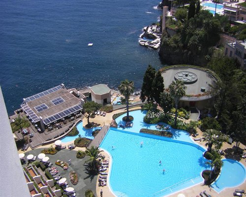 View of the outdoor swimming pool with sunshades alongside ocean.