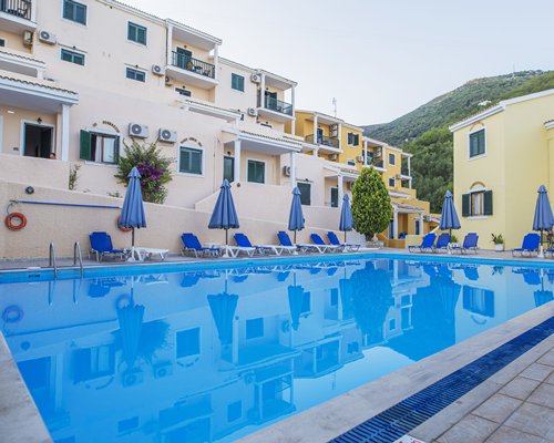 Outdoor swimming pool with chaise lounge chairs and sunshades alongside multiple unit balconies.