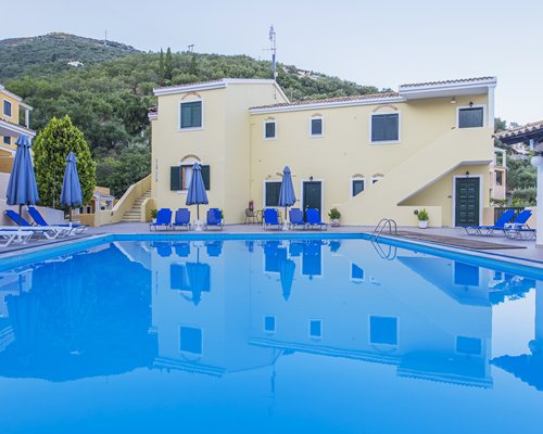 An outdoor swimming pool with chaise lounge chairs and sunshades alongside resort condos.