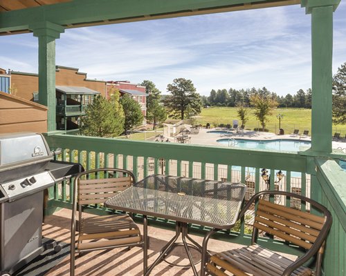 A balcony view of an outdoor swimming pool with patio furniture and a barbecue grill.