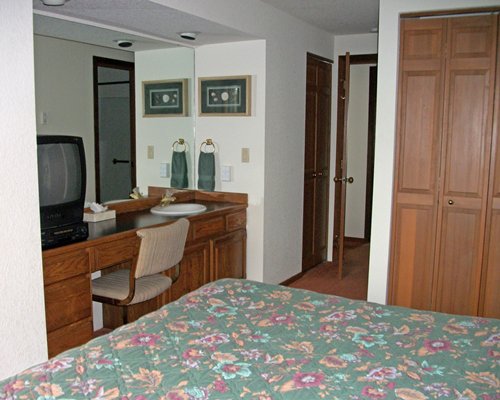 A well furnished bedroom with queen bed television and closed sink vanity.