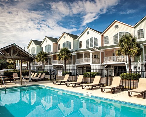 View of multiple units with outdoor swimming pool chaise lounge chairs and palm trees.
