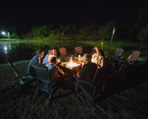 Guests enjoying lakeside dining around an open hearth at night.