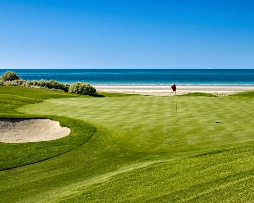 A GOLF COURSE PUTTING GREEN ALONGSIDE THE BEACH.